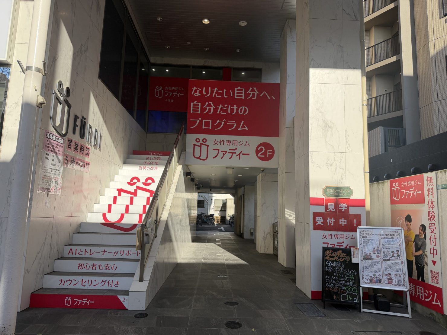 ファディー小岩店の入口。2階へ続く階段に「AIとトレーナーがサポート」「初心者も安心」「カウンセリング付き」と書かれている